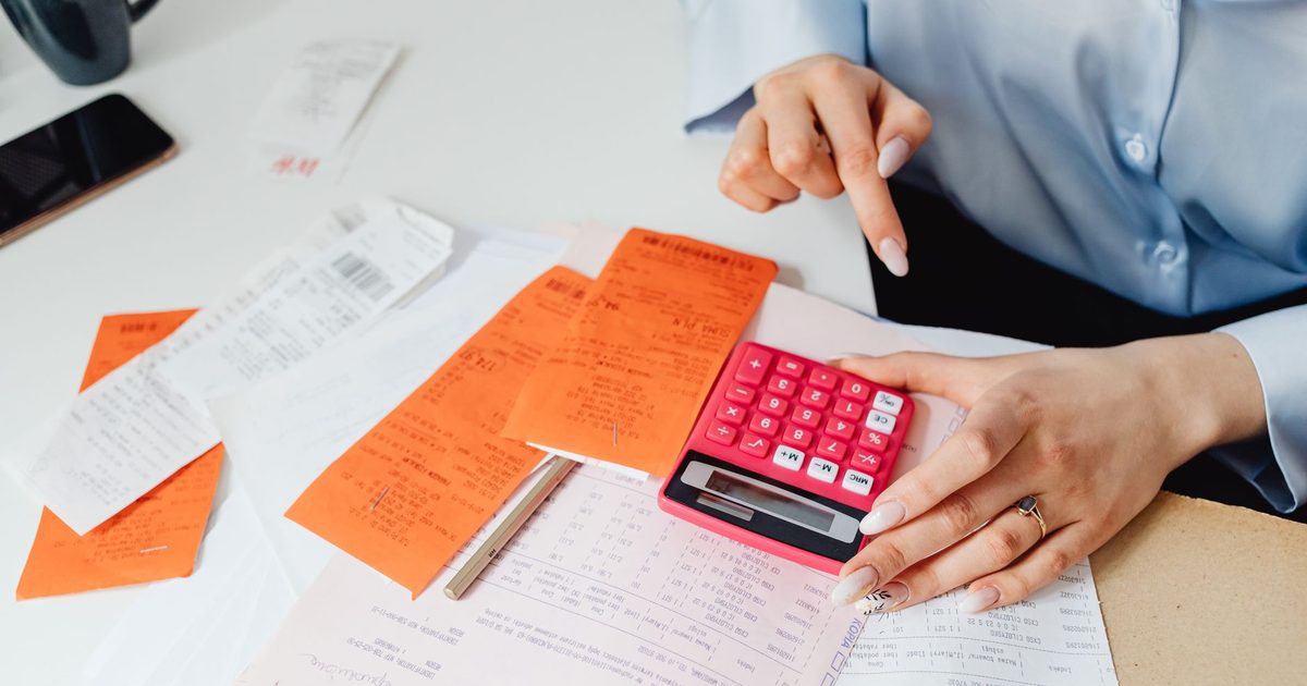 Mãos com calculadora, recibos e contas escritas à mão sobre a mesa