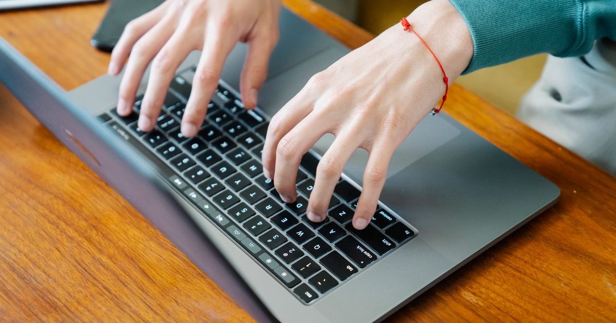 Mãos digitando no teclado de um laptop sobre uma mesa de madeira
