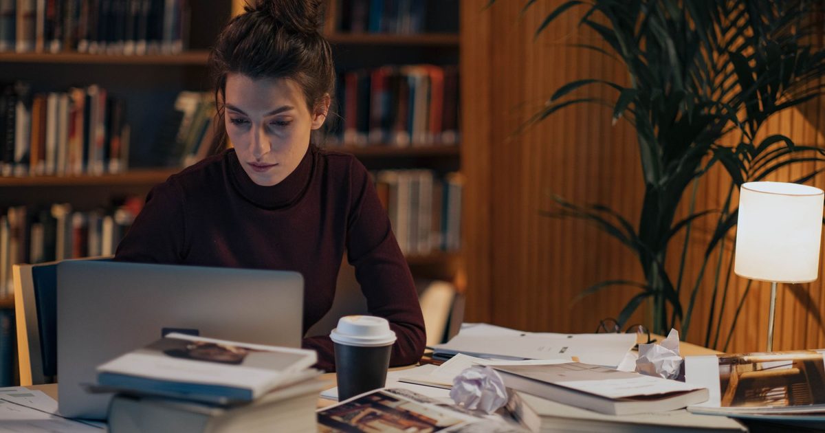 Mulher trabalhando numa mesa coberta de livros abertos e um laptop